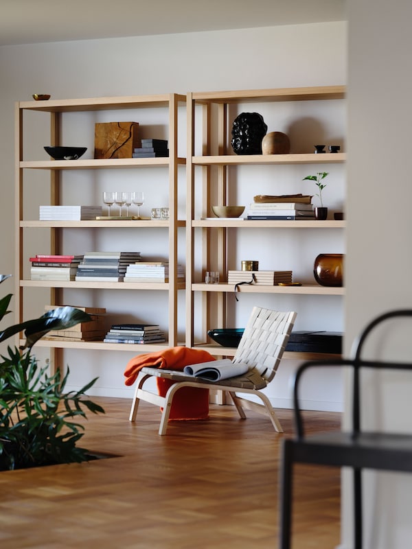 An oak veneer STOCKHOLM 2025 shelving unit against a white wall, with bowls, glasses, a tray, and other items on the shelves.