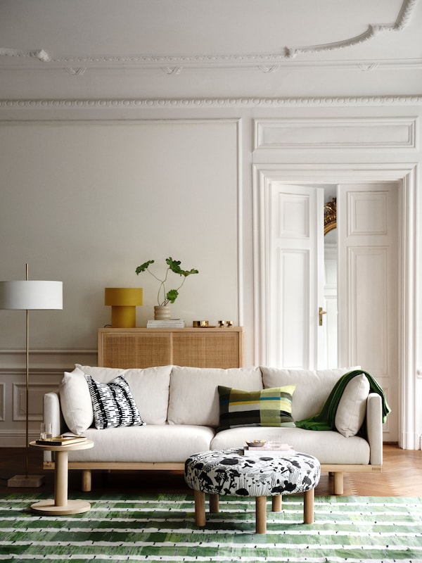A living room with a STOCKHOLM 2025 3-seat sofa, pillows and a throw resting on it, side table and pouffe on a rug in front.