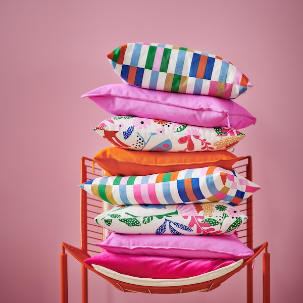 Pile of bright cushions in various colours including pink and orange as well as different patterns stacked on a chair.