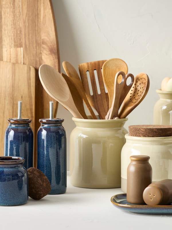 A blue BRUGDHAJ jar with a cork lid next to it is placed next to two blue BRUGDHAJ oil and vinegar bottles on a worktop.